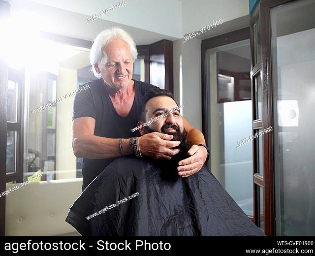 Hairstylist styling customer's beard in salon