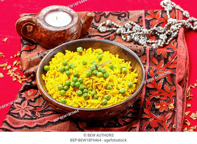 Indian cuisine: bowl of yellow rice with green peas on red background