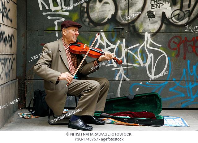 Elderly violinist playing for tips on a street in Florence, Italy. The graffiti on the wall behind is quite in contrast to the impeccable formal attire of the...