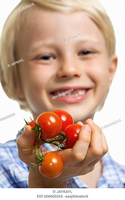 Close-up of a cute boy holding out a bunch of vine ripened organic cherry tomatoes. Isolated on white