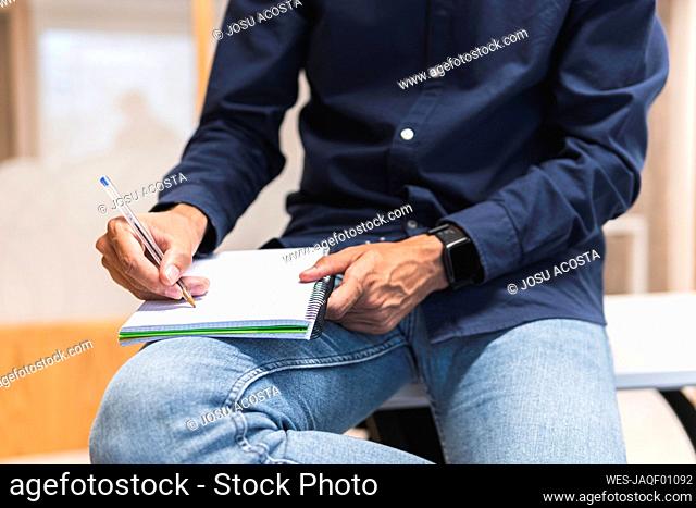 Hand of businessman writing in diary sitting on desk
