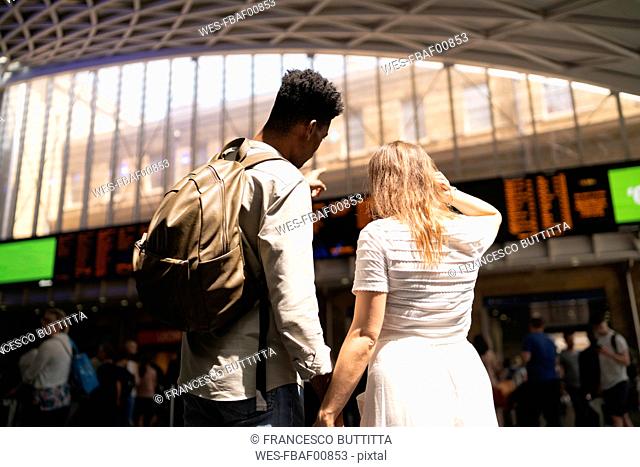 Back view of young couple looking at display panel of train station, London, UK