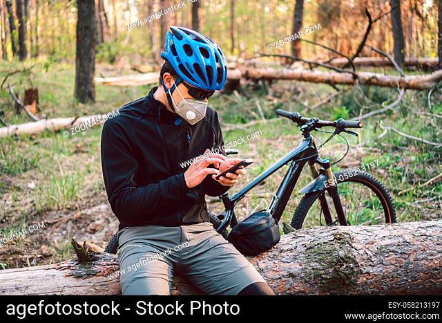 Male cyclist wearing respirator face mask with heavy duty protective filter, sitting in forest and uses phone. safety device for protect health