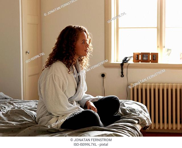 Young woman in bathrobe sitting on bed