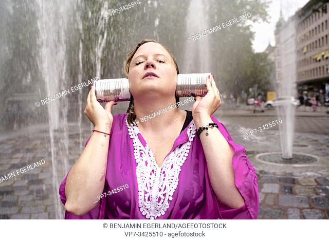 Woman covering ears with cans under fountain spray, Munich, Germany