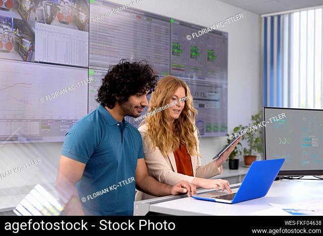 Businesswoman using laptop discussing with technician at desk in control room