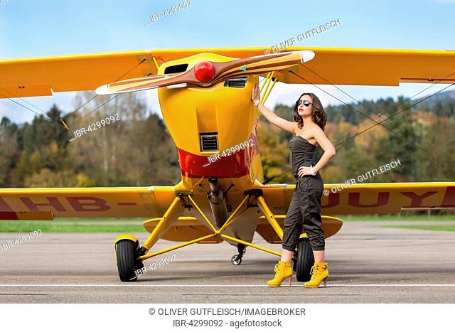 Young woman with sunglasses in overall and boots posing in front of double-decker airplane, fashion, lifestyle, photo shoot