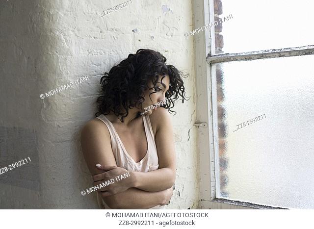 Sad young woman standing by the window looking away