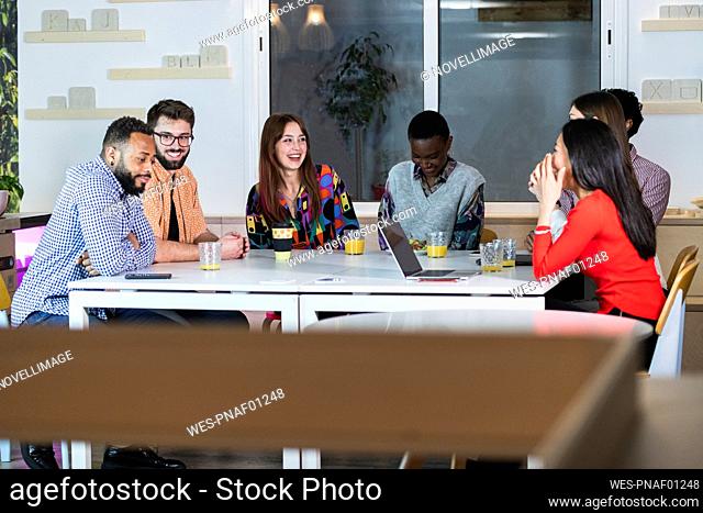 Multi ethnic coworkers smiling while sitting at table in cafeteria