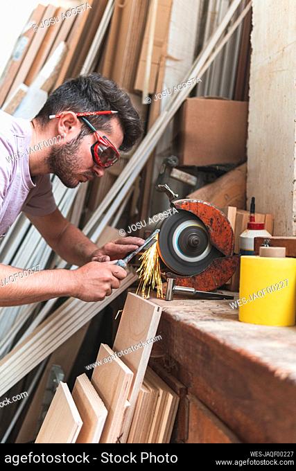Male craftsperson sharpening chisel on grinder while working in workshop