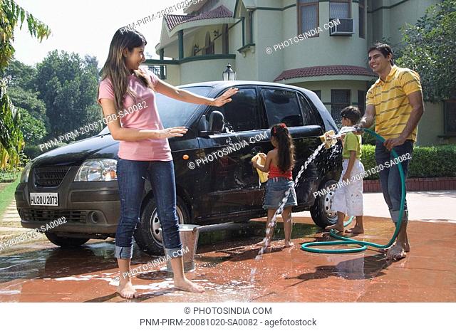 Man spraying water on his wife while his children washing a car, New Delhi, India