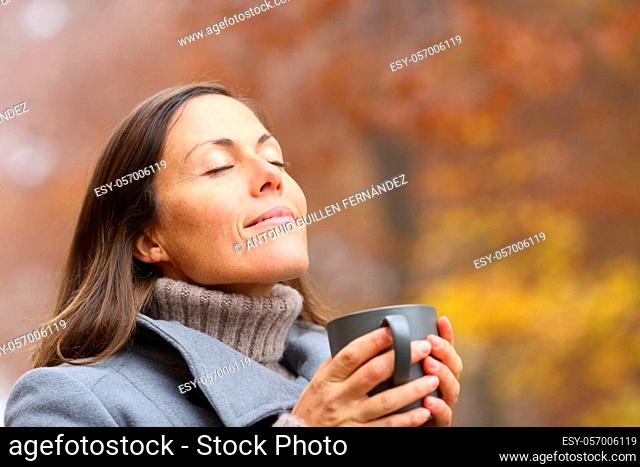 Relaxed adult woman holding coffee cup breathing fresh air in autumn in a forest