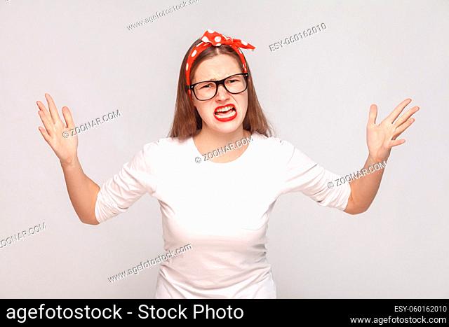 what do you want? portrait of unsatisfied angry emotional young woman in white t-shirt with freckles, black glasses, red lips and head band