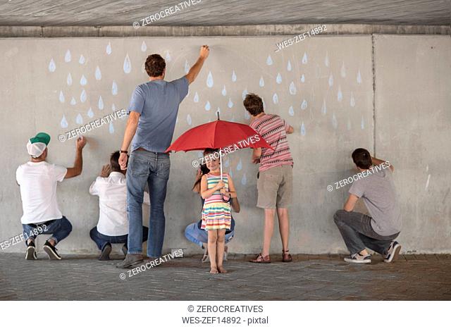 People drawing raindrops on concrete wall, little girl standing holding red umbrella