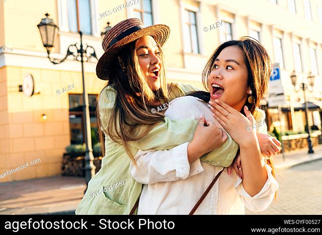Surprised woman looking at friend embracing from behind in city