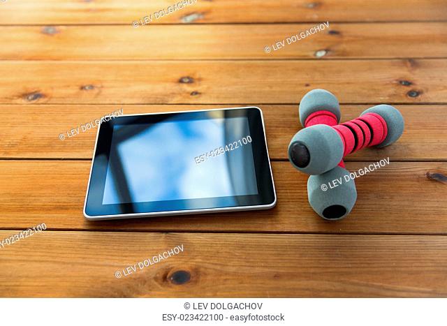 sport, fitness, technology and objects concept - close up of dumbbells and tablet pc computer on wooden floor