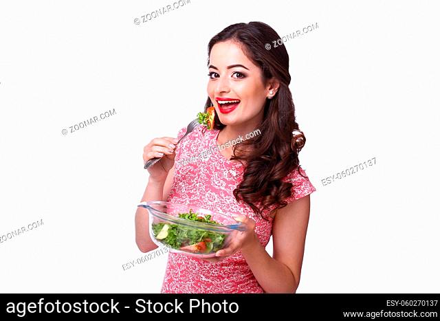 Beautiful brunette girl slices vegetables for salad sitting at the kitchen table on a isolated white background
