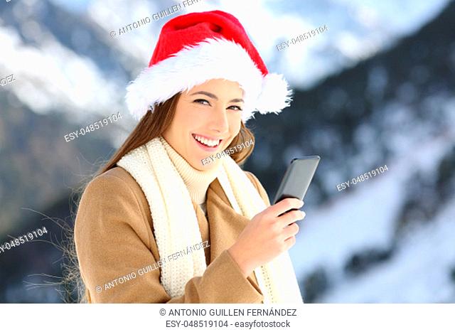 Happy woman holding a smart phone on christmas holidays in the snowy mountain