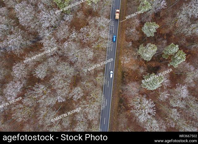 Germany, Bavaria, Drone view of cars driving along asphalt road cutting through Steigerwald forest in winter