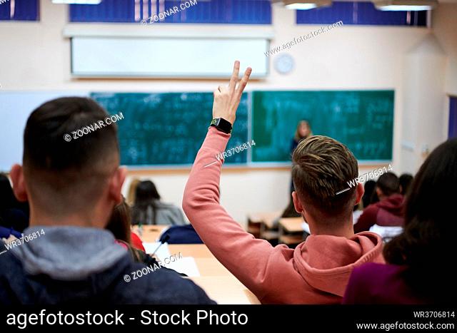 The student raises his hands asking a question in class in college. The concept of education