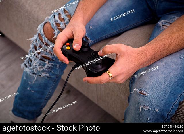 Closeup of hipster man in jeans playing computer games. Young man holding joystick for playing computer games on laptop computer or television