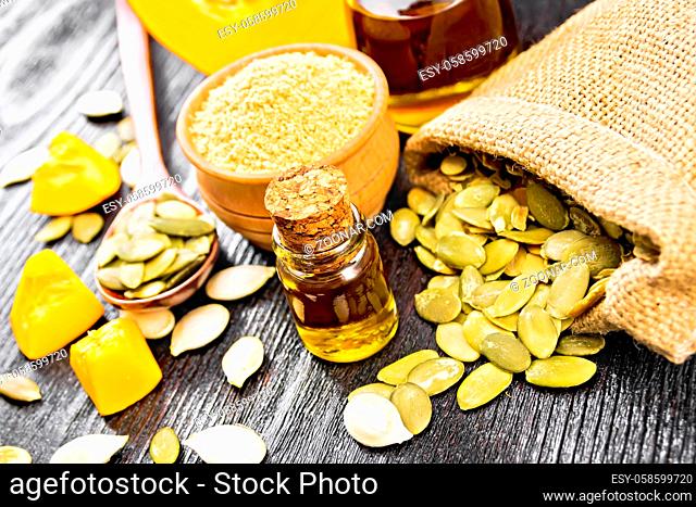 Pumpkin oil in vial and a jar, flour in a bowl, seeds in a spoon and bag, slices of vegetable on wooden board background