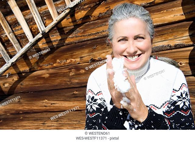 Italy, South Tyrol, Seiseralm, Senior woman holding snow in hands, smiling, portrait