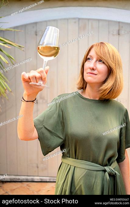 Thoughtful mature woman looking at white wine in front of wall