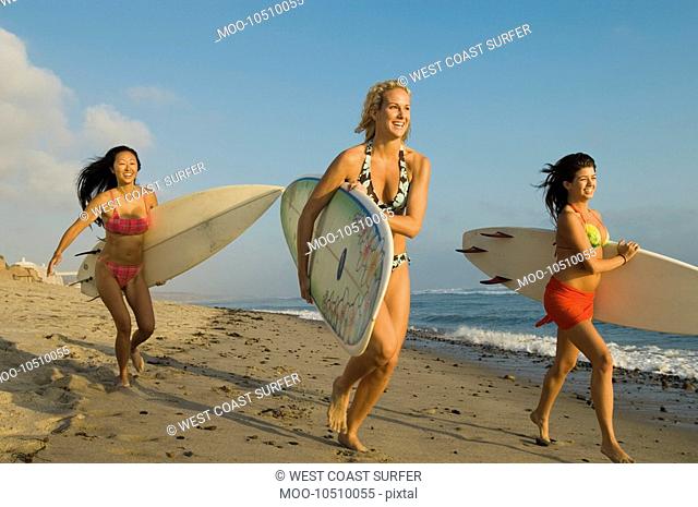 Three female surfers carrying surfboards running on beach