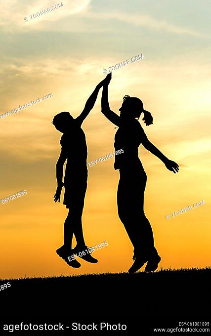 A boy and a teen girl jump up at sunset and give each other a high five