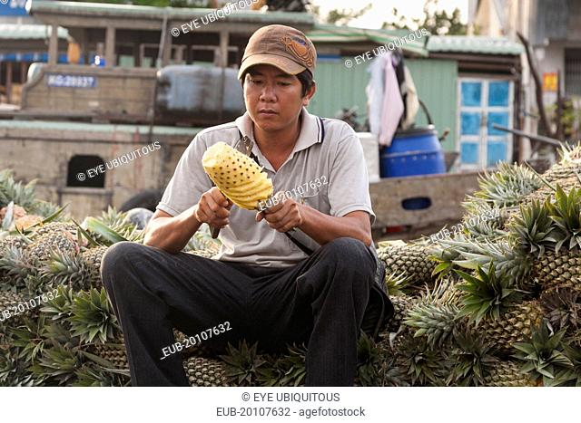 Man cutting a pineapple in the floating market at Cai Rang near Can Tho