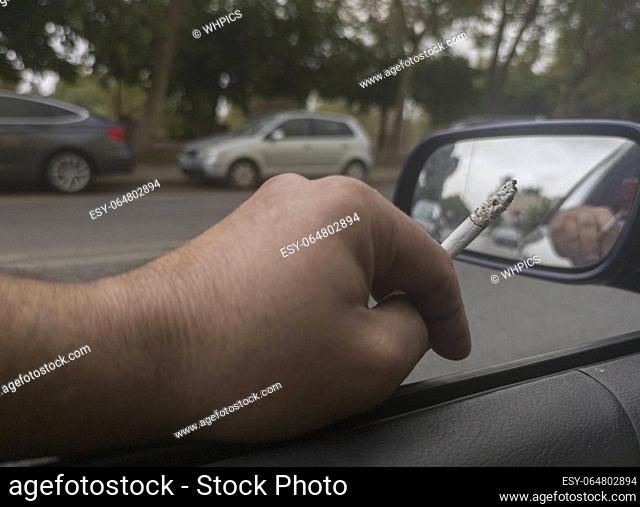 Man smoking and driving with the window down. Cause of distracted driving accidents concept