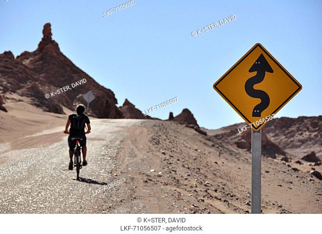 Man cycling and crossing traffic sign at road, Valle de la Luna, Valley of the moon, Atacama desert, Reserva Nacional Los Flamencos, Region de Antofagasta