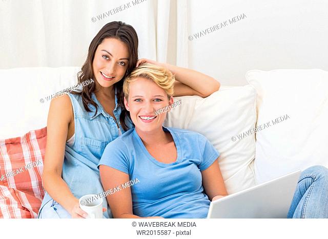 Portrait of smiling homosexual couple sitting on couch and using laptop