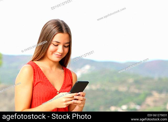 Happy teen in red checking phone outdoors