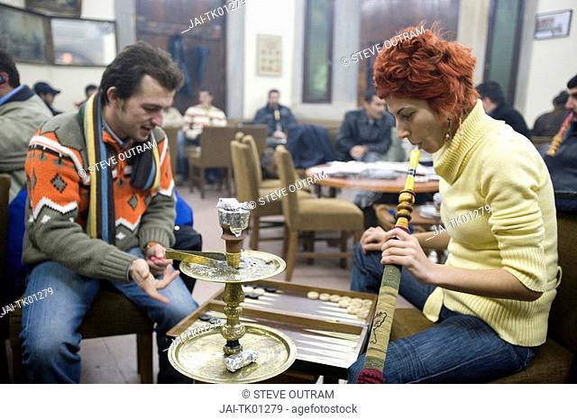 Young Turkish couple playing Backgammon and smoking Nargiles Bubble Pipes inside Corlulu Ali Pasha traditional cafe, Istanbul, Turkey. MR and PR
