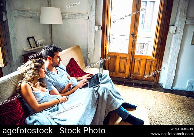 Young couple sitting on couch at home watching laptop