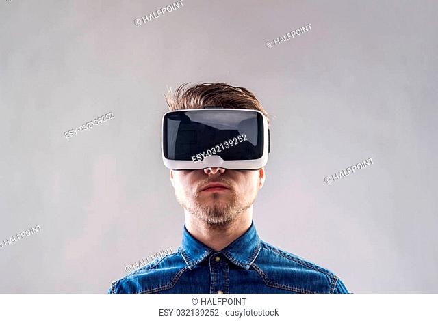 Hipster man in denim shirt wearing virtual reality goggles. Studio shot on gray background
