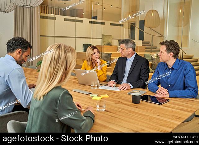 Businessman and businesswoman discussing while sitting with colleagues in board room