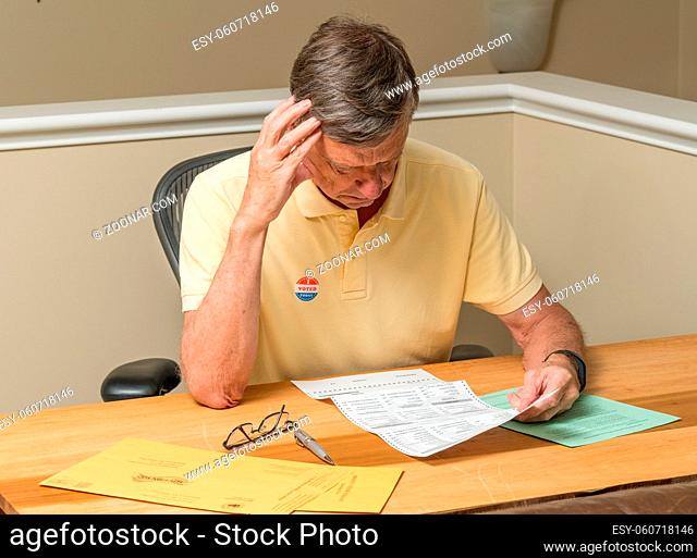 Senior caucasian man seated at home desk and completing the mail-in or absentee ballot for the 2020 presidential election