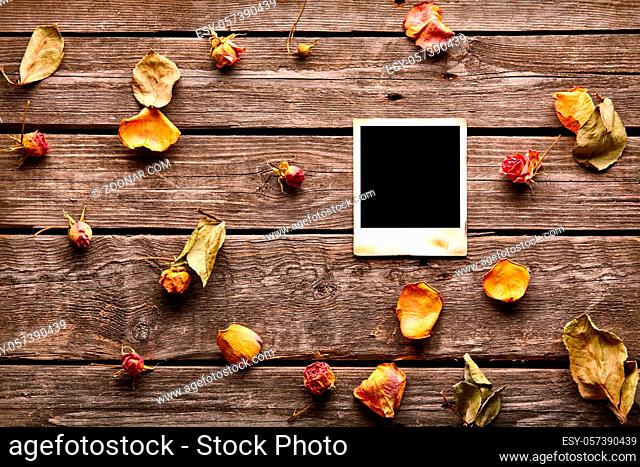 Blank instant photo with roses and petals. On old wood background
