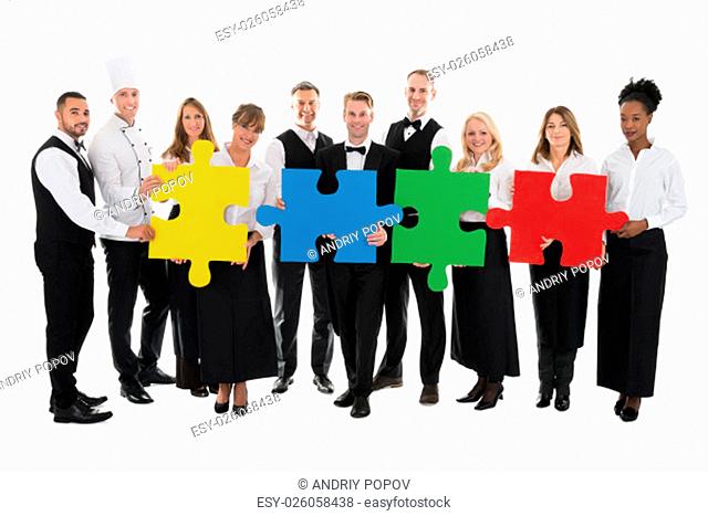Portrait of confident restaurant staff joining jigsaw pieces against white background