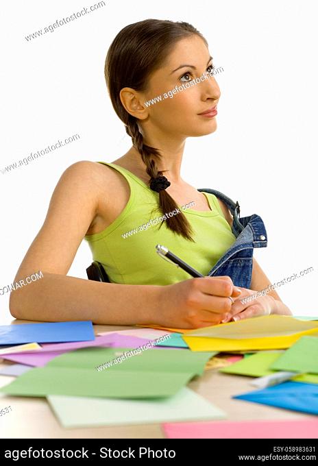 Young, beautiful woman sitting, smiling and writing a letter. Thinking of something. White background