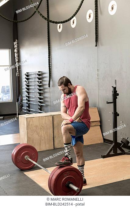 Mixed Race man resting on barbell in gymnasium
