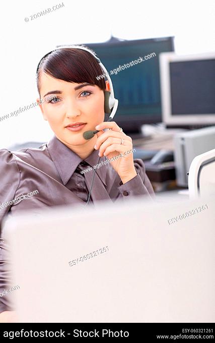 Young female customer service operator talking on headset, holding the microphone
