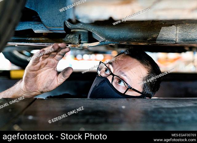 Close-up of male mechanic wearing mask examining car in garage