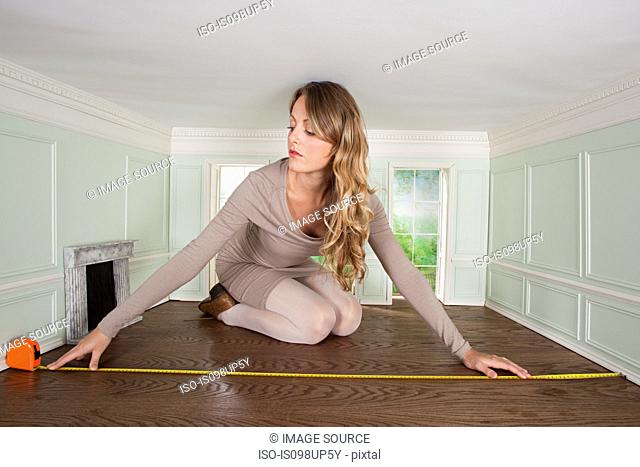 Young woman in small room measuring the floor