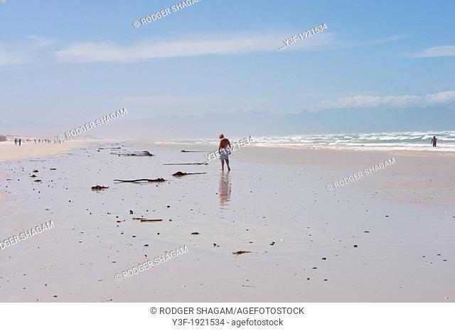 A man walks on the beach, reflected in the wet mud on an out going low tide. Muizenberg beach. Cape Town, South Africa