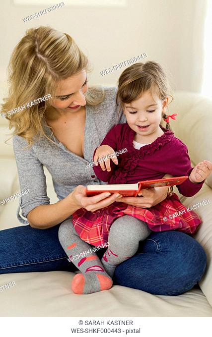 Little girl sitting on her mother's lap watching a book