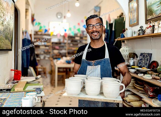 Smiling male artist holding potteries while standing in workshop